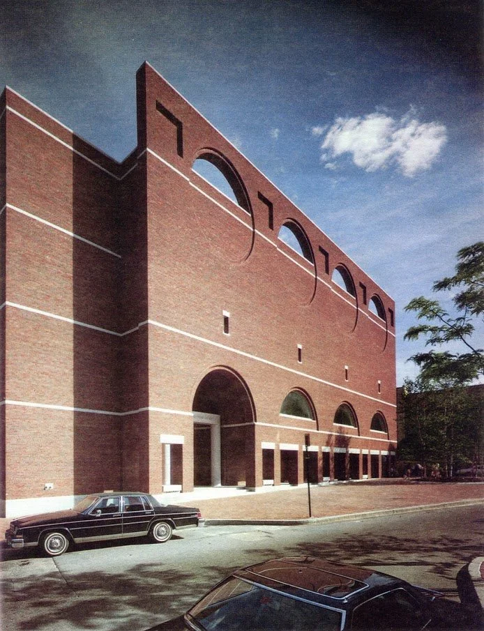 Rectangular brick building with arched openings and circular windows.