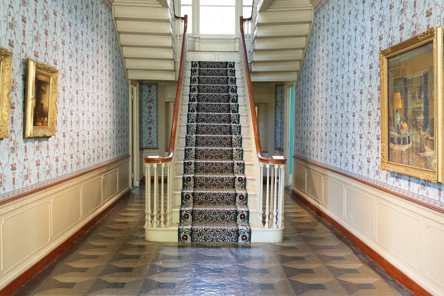 Ornate staircase with patterned carpet and framed art in an elegant hallway.